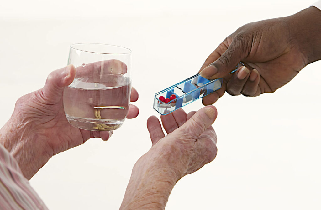 "A hand holding medicines assisting an older adult take their medications."