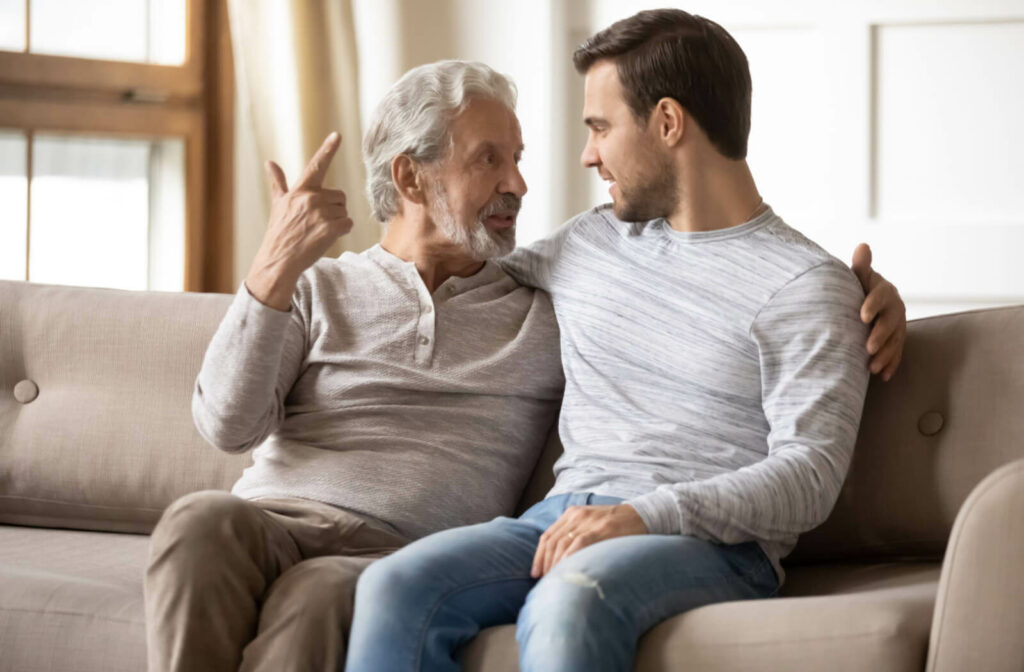 A man and and his senior father having a conversation in a brightly lit living room while sitting on the co