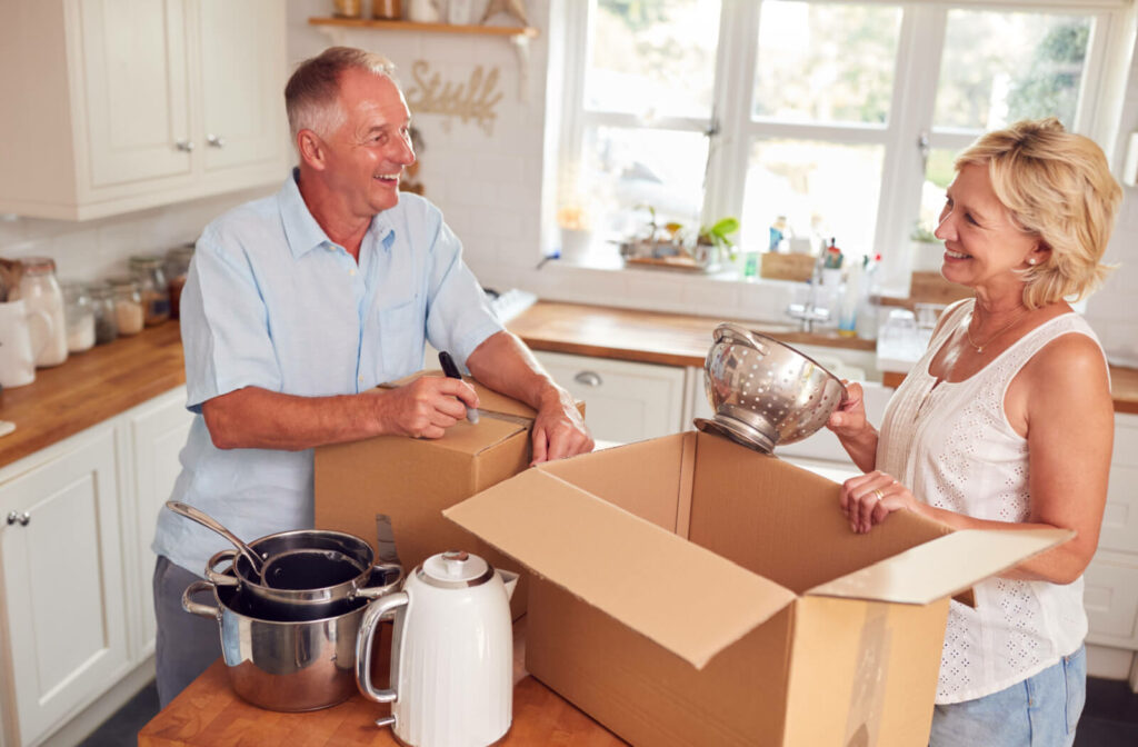 A senior couple downsizing by putting extra cooking utensils in a cardboard box.