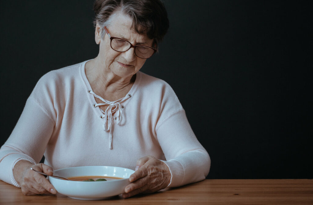 A senior woman against a black background showing no excitement about having soup.