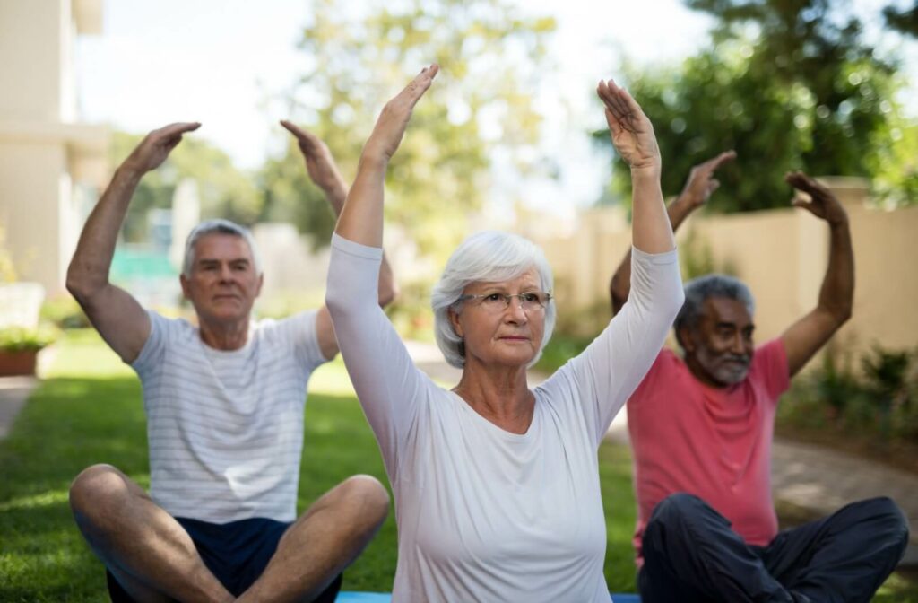 A group of older adults doing yoga outdoors with their hands raised while sitting.