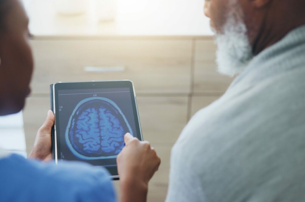 A close-up image of a healthcare professional showing an older adult a brain image scan.