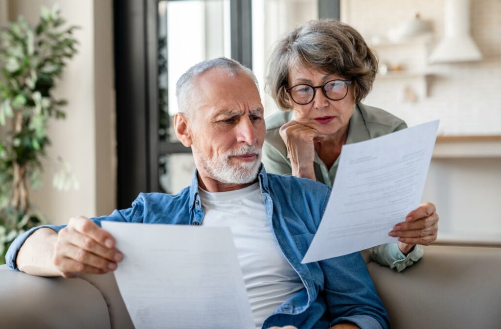 An elderly couple reviews documents together on a sofa, looking confused and concerned