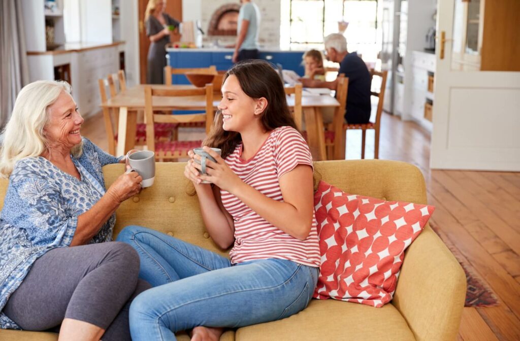 Older adult and younger adult sitting on a couch, smiling and having a conversation over coffee in a cozy living room