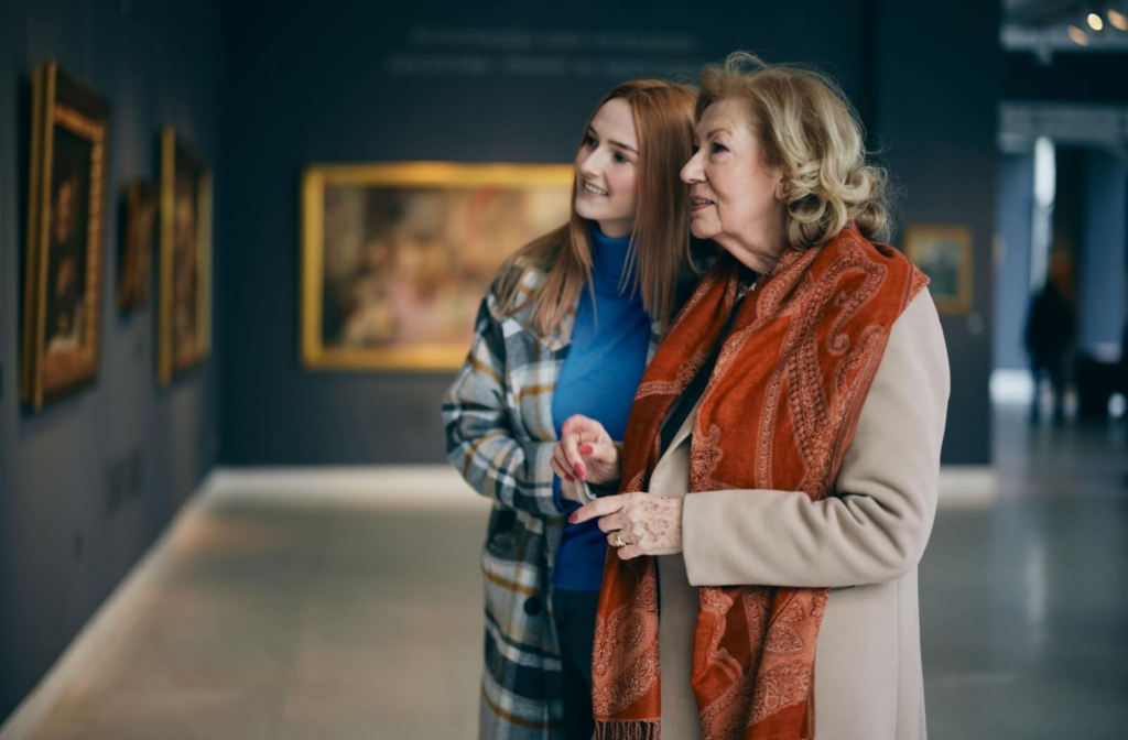 An adult and their senior grandparent look at the paintings in an art gallery in Cleveland.
