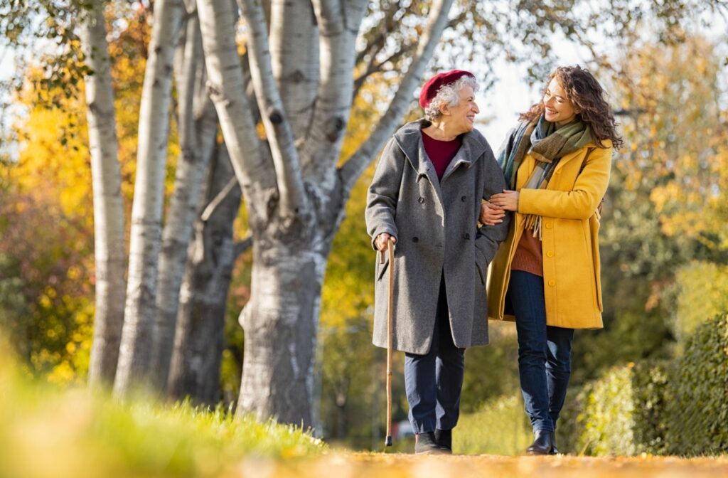 An adult walks with their senior grandparent in a Cleveland park during autumn, wearing yellow and gray winter coats