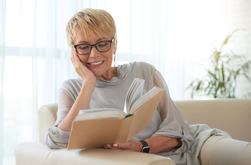 a senior woman reads a book while sitting on a couch