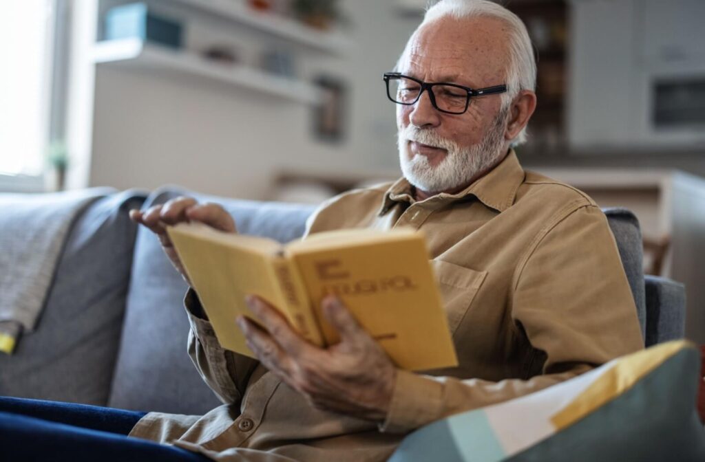 a senior man sits on a couch reading a novel
