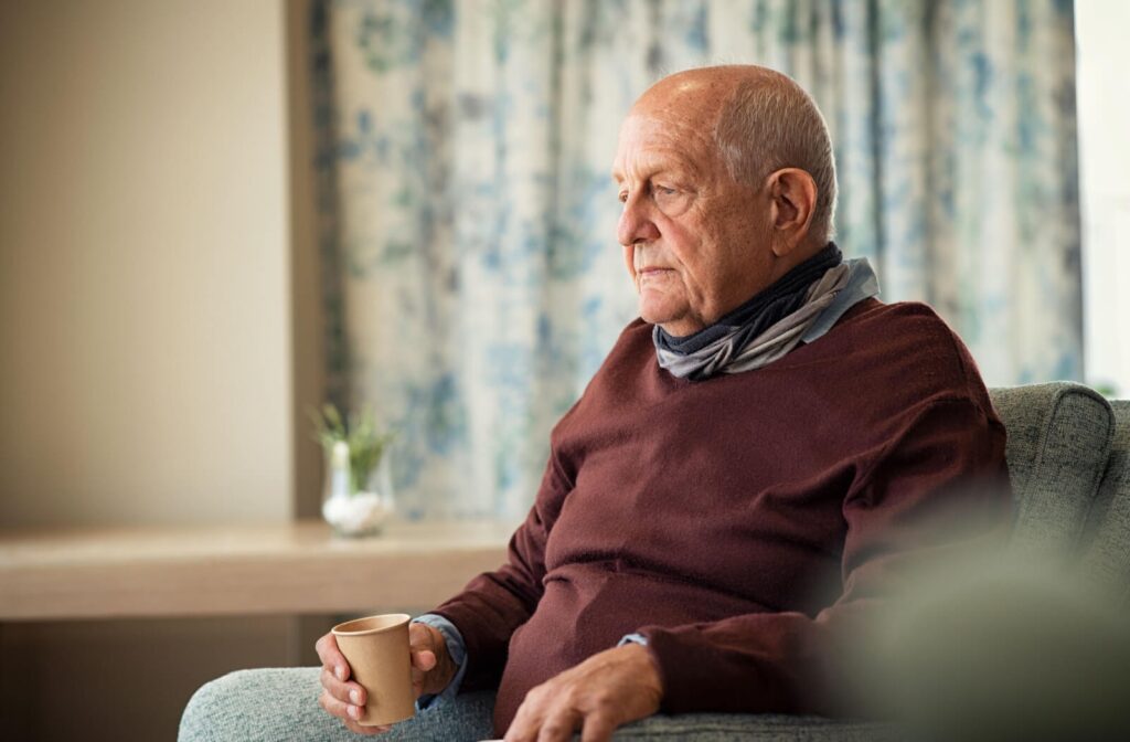 An older adult sits on a couch with a cup of water